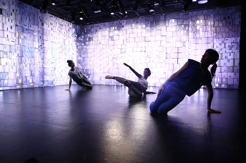 Three dancers lean on their knees on the floor. A purple hue casts on them.